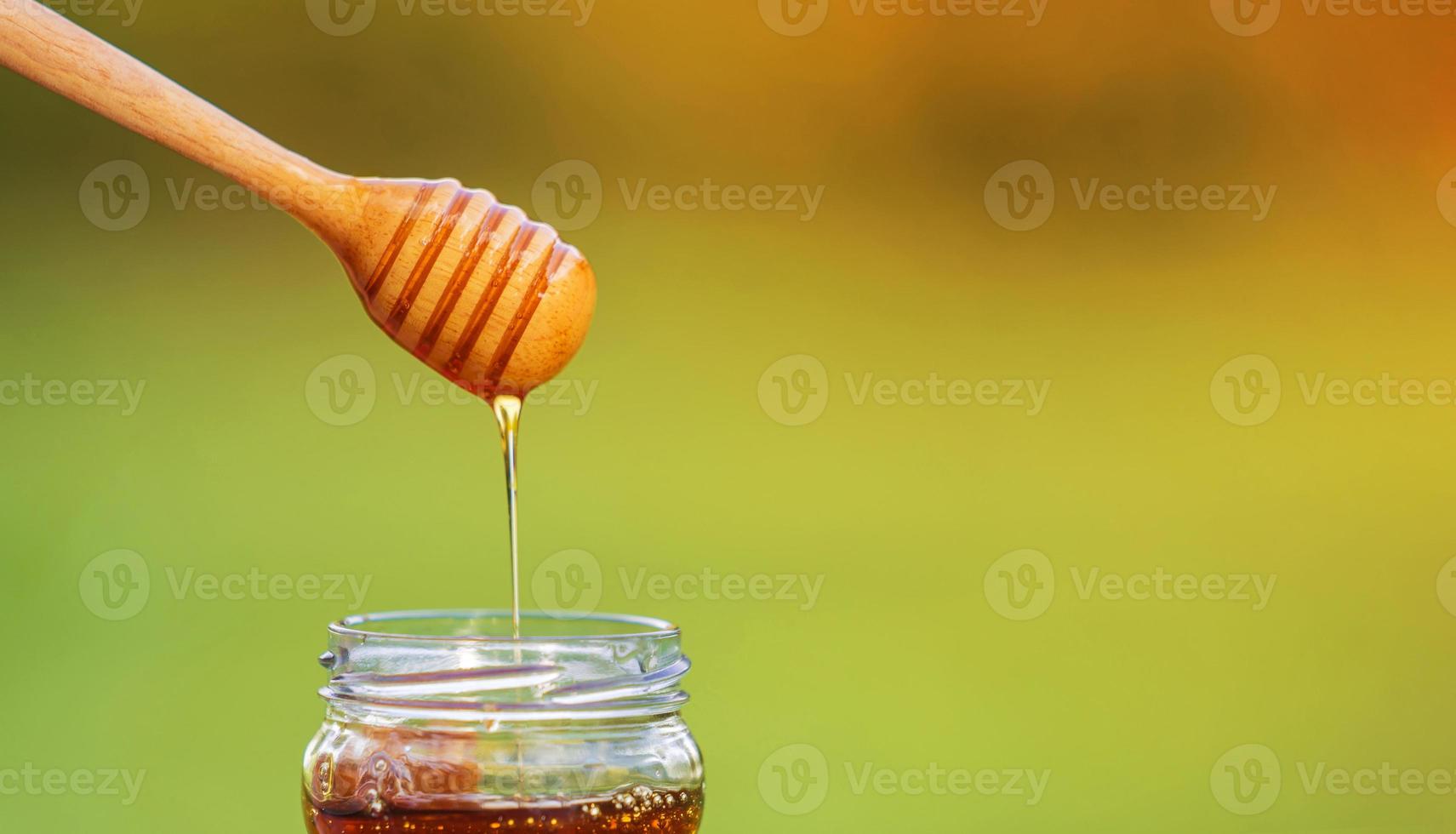 Honig tropft von Honigschöpflöffel auf natürlichem Hintergrund foto