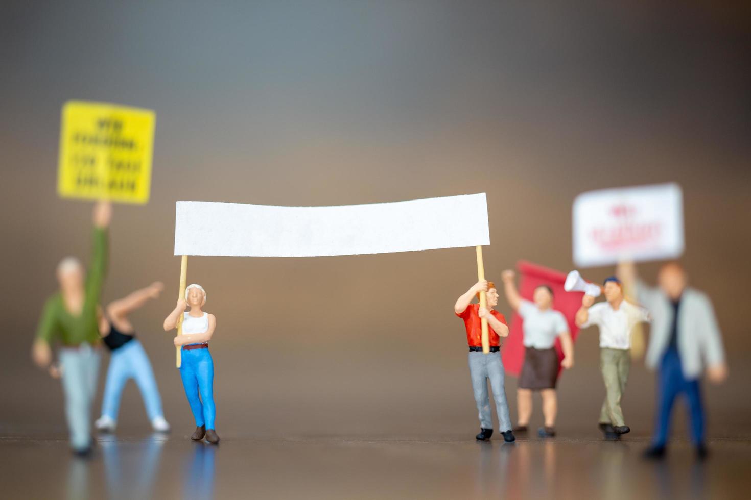 Miniaturmenge von Demonstranten, die ihre Hände heben und auf einem hölzernen Hintergrund schreien foto