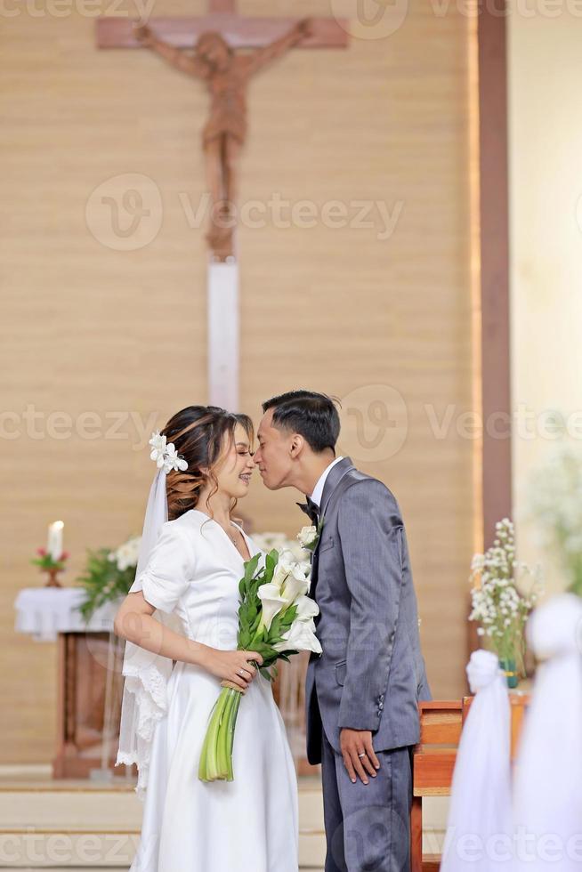 Braut und Bräutigam berühren Nasen nach Hochzeit Gelübde mit Kreuz Hintergrund im das Kirche, Neu Reise hat begann foto