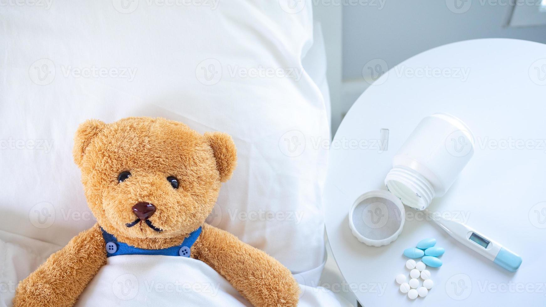 das Teddy Bär ist krank im das Bett Nächster zu ihn. Dort ist Medikament, Thermometer warten zu Sein behandelt. foto