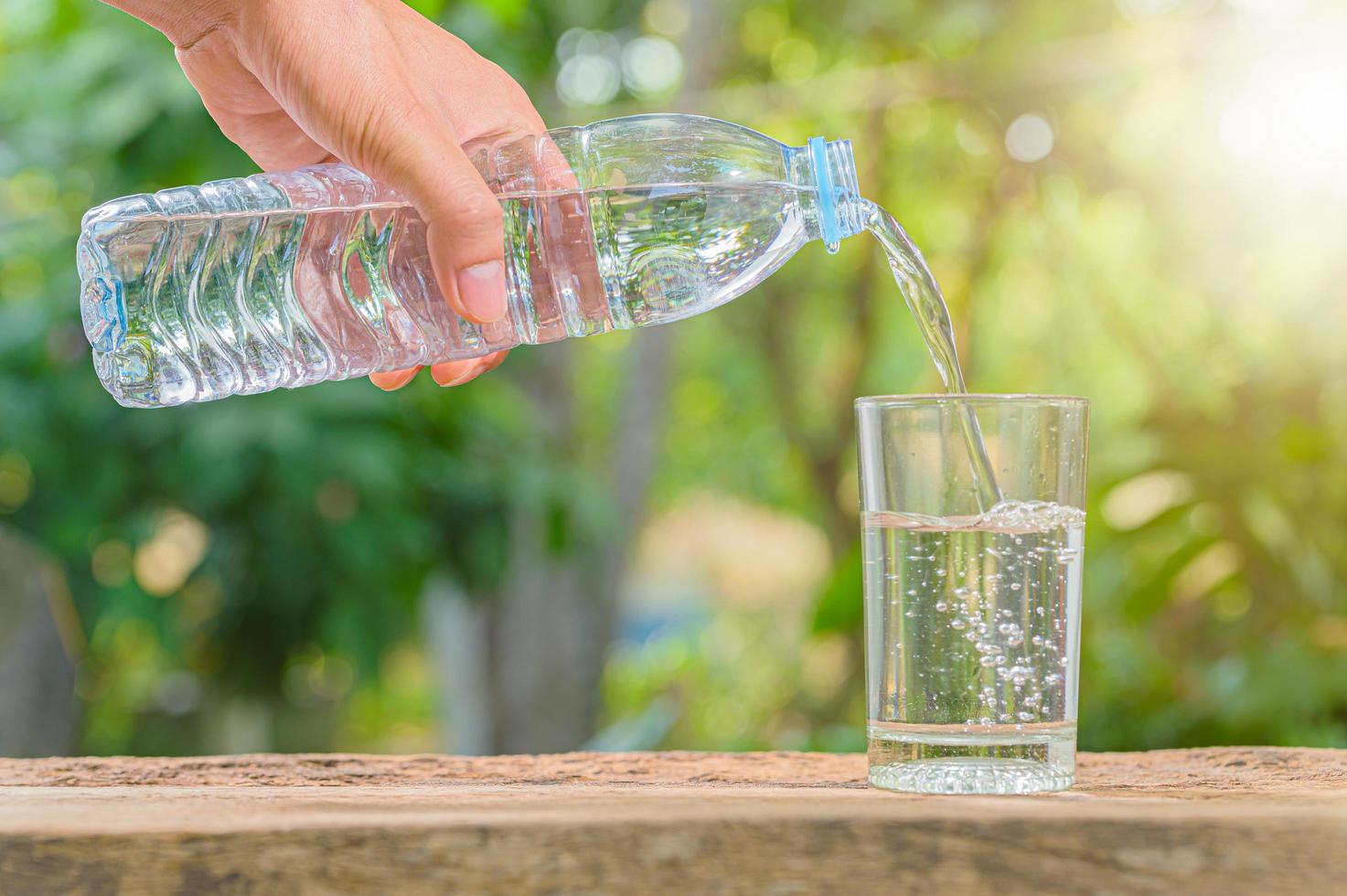 Flasche Trinkwasser und Glas mit natürlichem Hintergrund foto