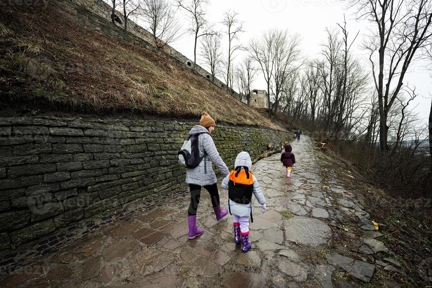 Mutter und Kinder gehen oben das nass Pfad zu ein uralt mittelalterlich Schloss Festung im Regen. foto