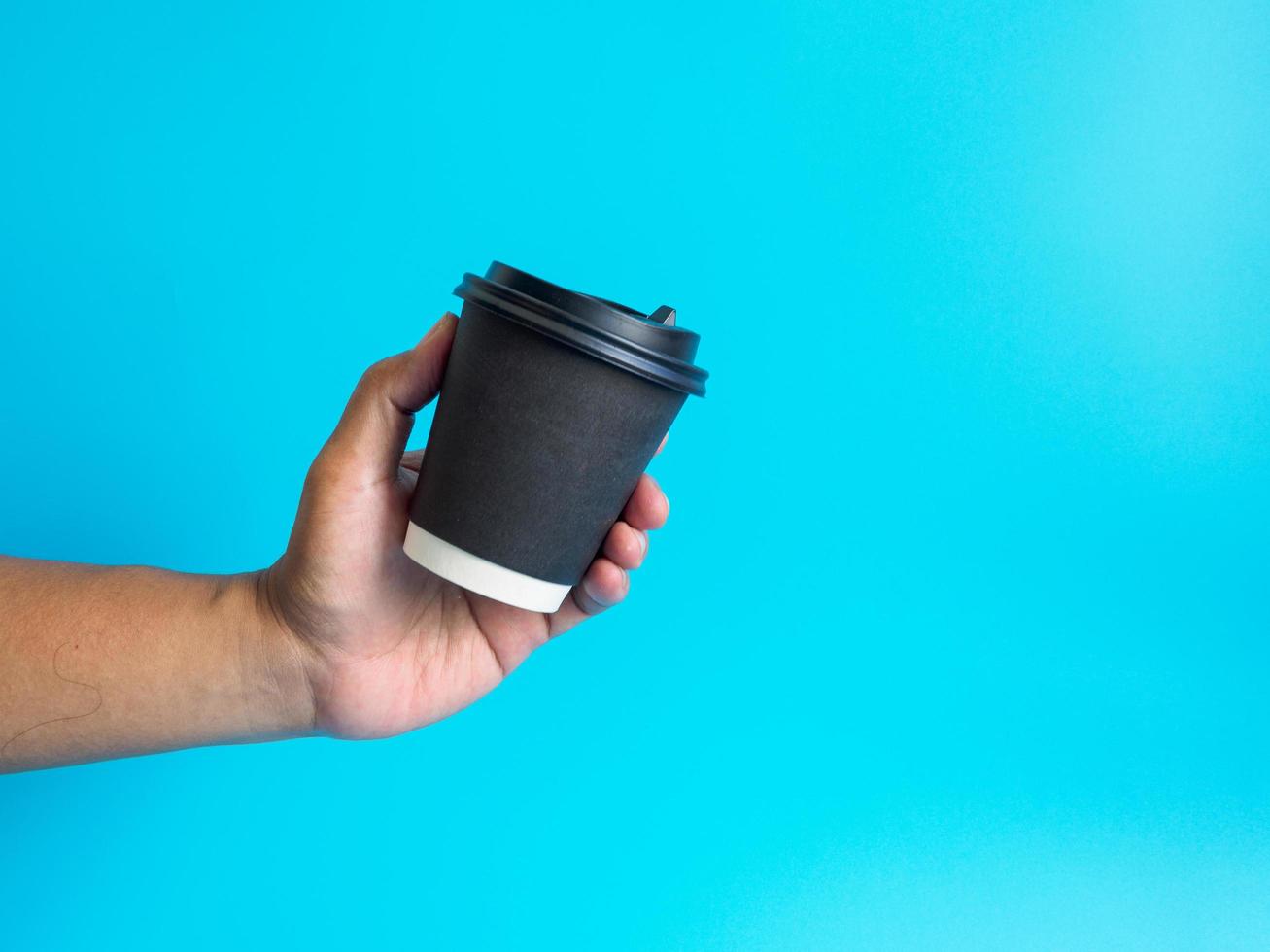 Nahansicht jung Erwachsene Mann Hand halten Weiß Tasse Papier von Kaffee heiß trinken bereit zu trinken erfrischend. Aroma Erwachen frisch zu Arbeit platziert auf ein Blau isoliert Hintergrund. Punkt von Aussicht Schuss. foto