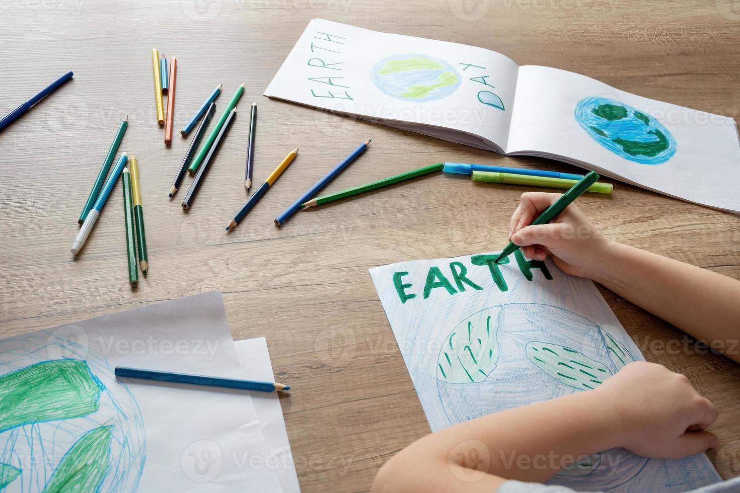 ein Kind beim Schule beim das Tabelle zeichnet das Planet Erde mit ein Welt Karte mit mehrfarbig Bleistifte und Filzstift Stifte auf Weiß Papier. Frieden und Erde Tag Konzept. foto