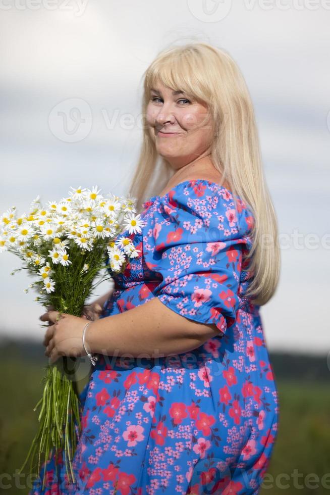 schön Plus Größe Frau mit Weiß Haar im ein Sommer- Kleid posieren draußen mit Gänseblümchen. mollig Mädchen im ein Wiese mit Blumen. foto