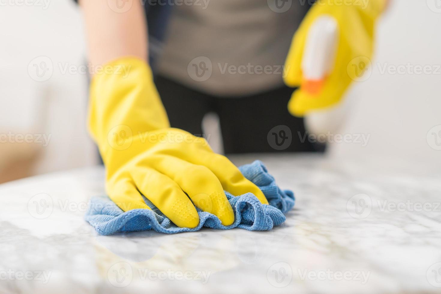 Reinigung Hygiene, schließen oben Hand von Dienstmädchen, Kellnerin Frau tragen Gelb schützend Handschuhe während Reinigung auf Holz Tisch, verwenden Blau Lappen abwischen zu Staub und sprühen im Restaurant. Hauswirtschaft aufräumen, sauberer foto