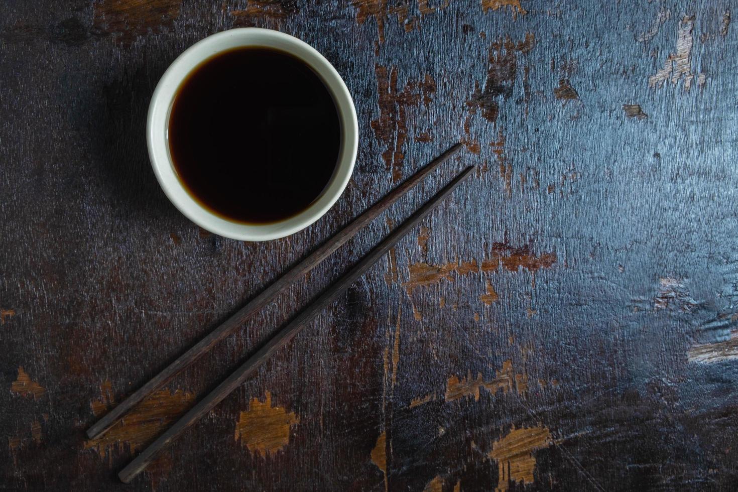 Tasse Sojasauce mit einem Paar Essstäbchen auf einem dunklen Holzhintergrund foto