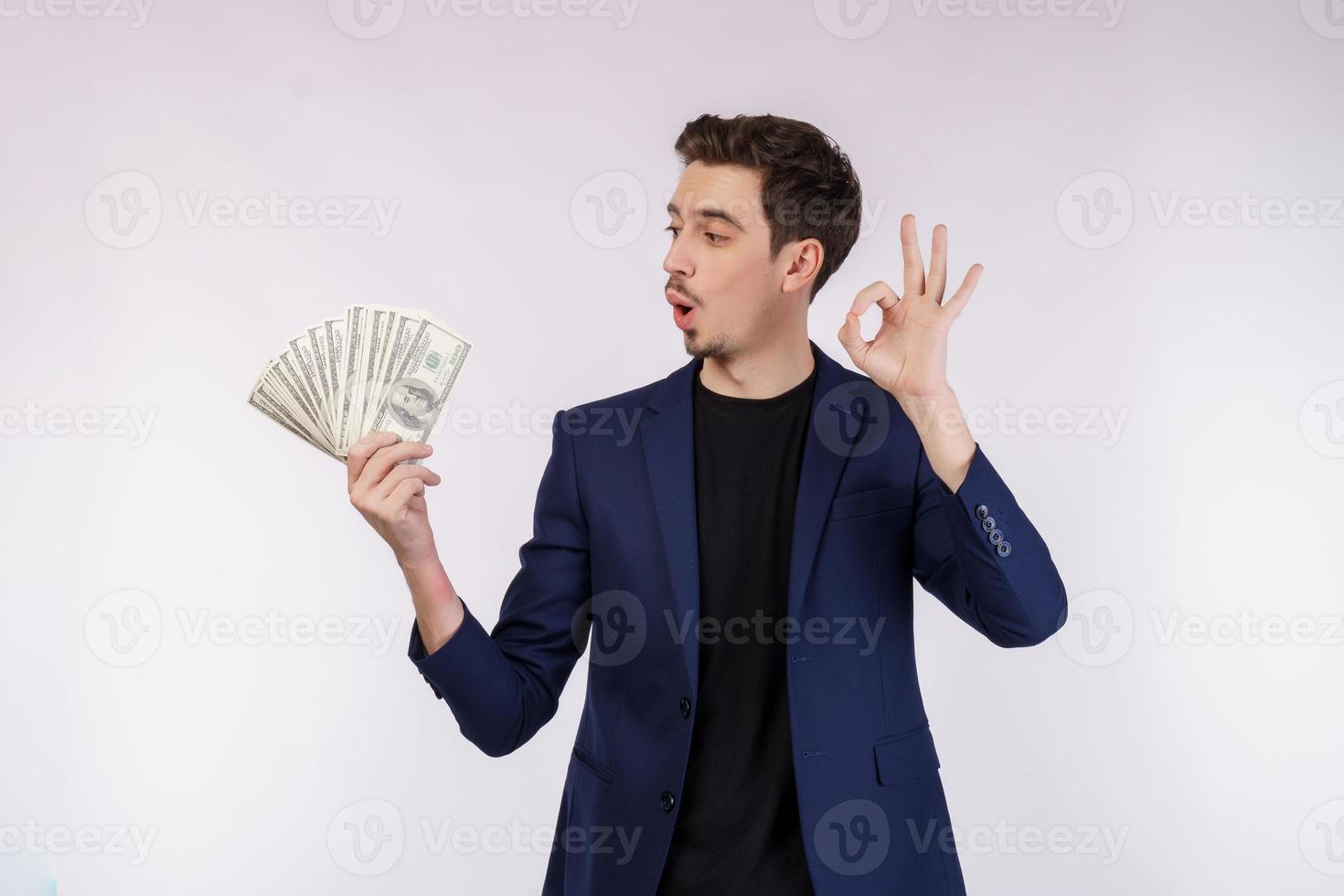 Porträt eines fröhlichen Mannes, der ein ok-Zeichen zeigt und Geld auf weißem Hintergrund hält foto