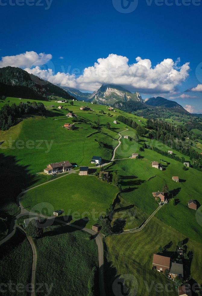 schweizerisch Wiese Felder mit Häuser und Berge, im wolkig Wetter foto