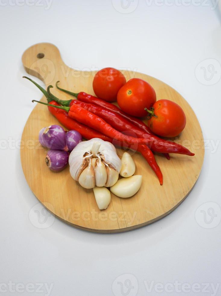 Knoblauch, Chili, rot Zwiebel und Tomaten auf ein hölzern Untersetzer, hoch Winkel Schuss. foto