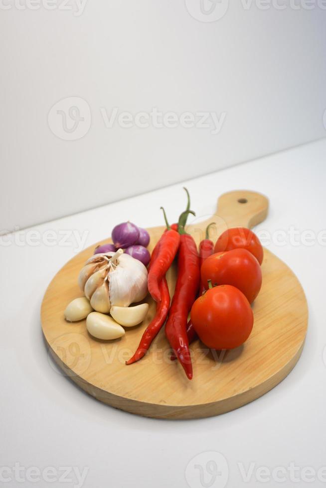 Knoblauch, Chili, rot Zwiebel und Tomaten auf ein hölzern Untersetzer, hoch Winkel Schuss. foto
