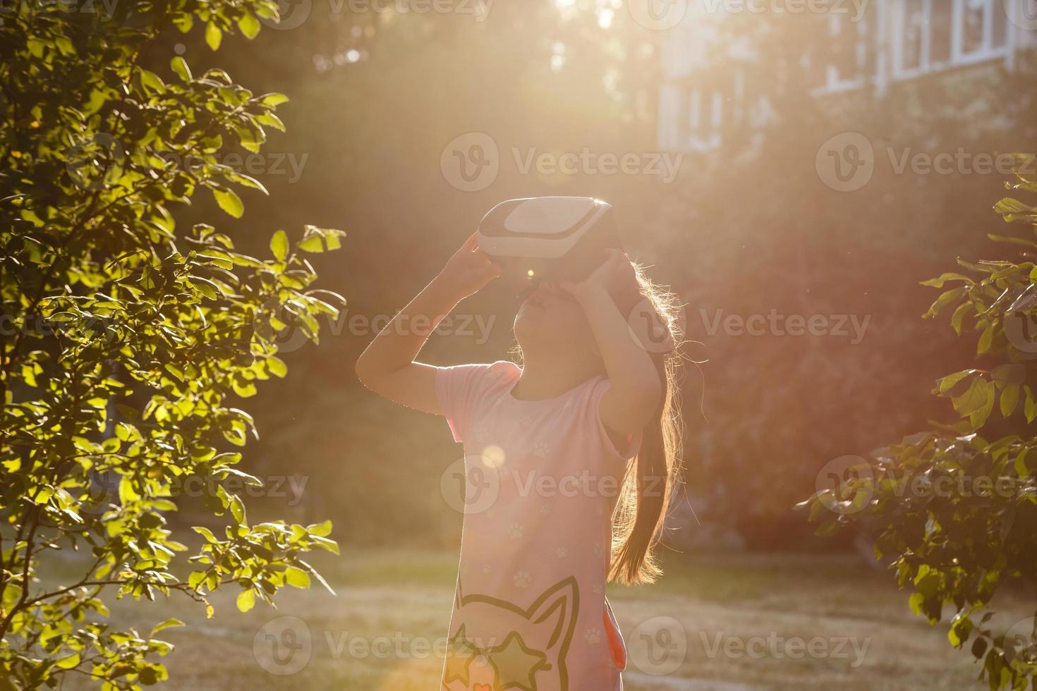 spielerisch wenig Mädchen mit virtuell Wirklichkeit Brille draussen im Sommer- Park. Kind suchen im vr Brille. Kind haben Spaß erleben 3d Gadget Technologie. foto