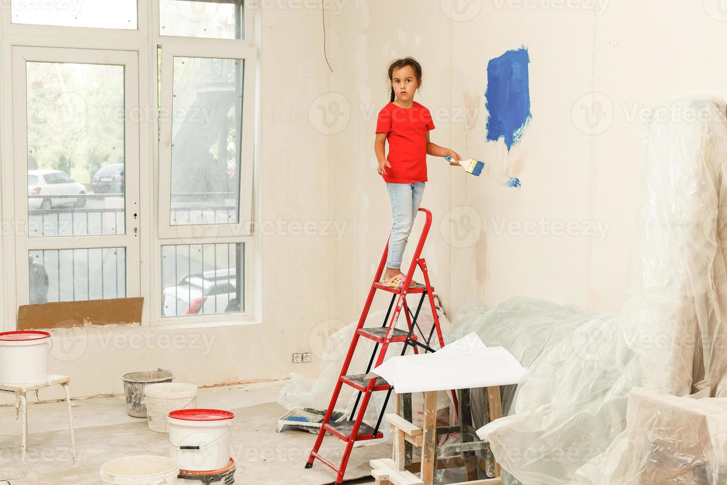 Reparatur im das Wohnung. glücklich Kind Mädchen Farben das Mauer mit Blau Farbe foto