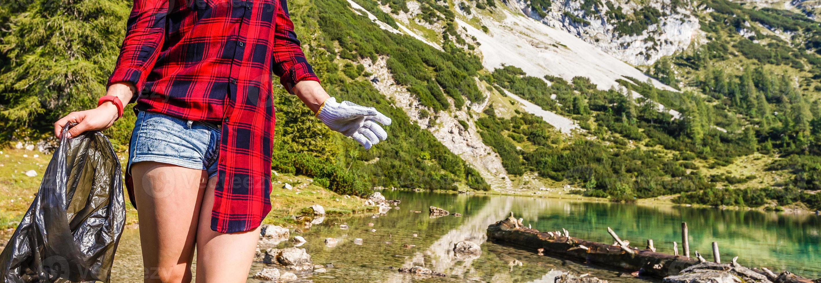 Glück Schönheit jung Touristen lächelnd mit Hand halten Paket in der Nähe von das alpin See Gipfel, Sommer- Ferien reinigt Müll foto