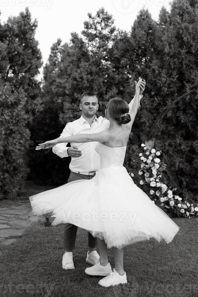 das zuerst tanzen von das Bräutigam und Braut im ein kurz Hochzeit Kleid auf ein Grün Wiese foto