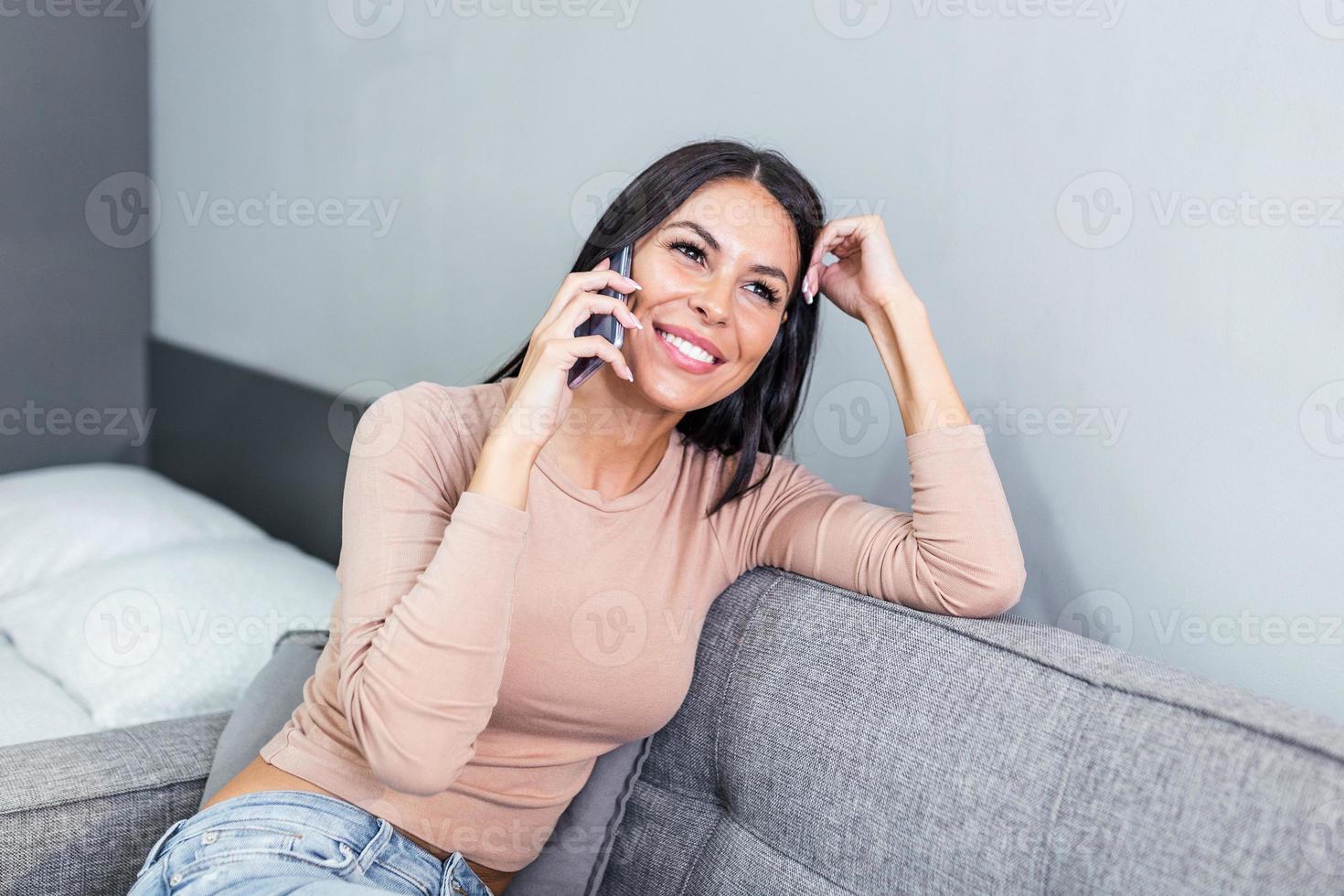 lächelnd schön Frau reden auf das Telefon beim heim, glücklich jung Mädchen hält Handy Herstellung antworten Forderung, attraktiv Mädchen haben angenehm Konversation chatten durch Handy, Mobiltelefon mit Freund foto