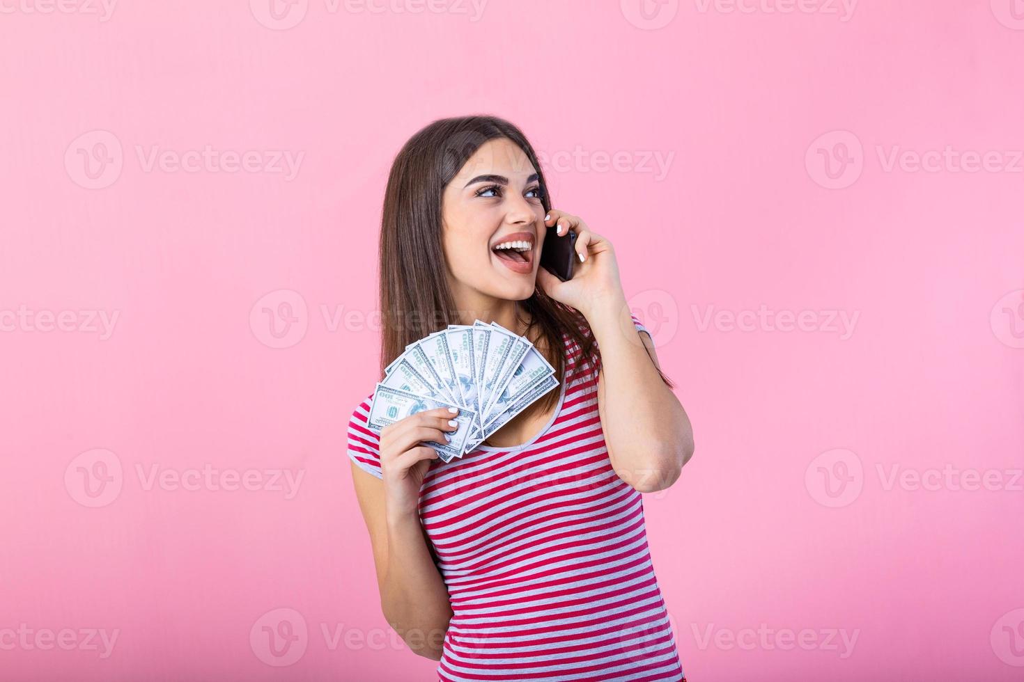 Bild einer schockierten, überraschten, schreienden jungen, hübschen Frau, die isoliert über rosafarbenem Wandhintergrund mit einem Handy posiert, das Geld hält. foto