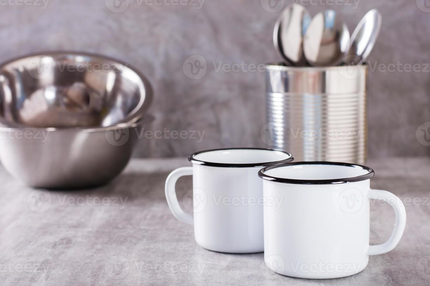 zwei Weiß leeren Metall Tassen, Löffel im ein können und Metall Platten auf ein grau Hintergrund foto