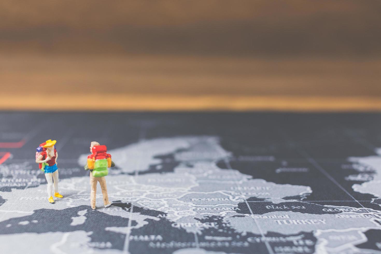 Miniatur-Rucksacktouristen, die auf einer Weltkarte, einem Tourismus- und Reisekonzept spazieren gehen foto