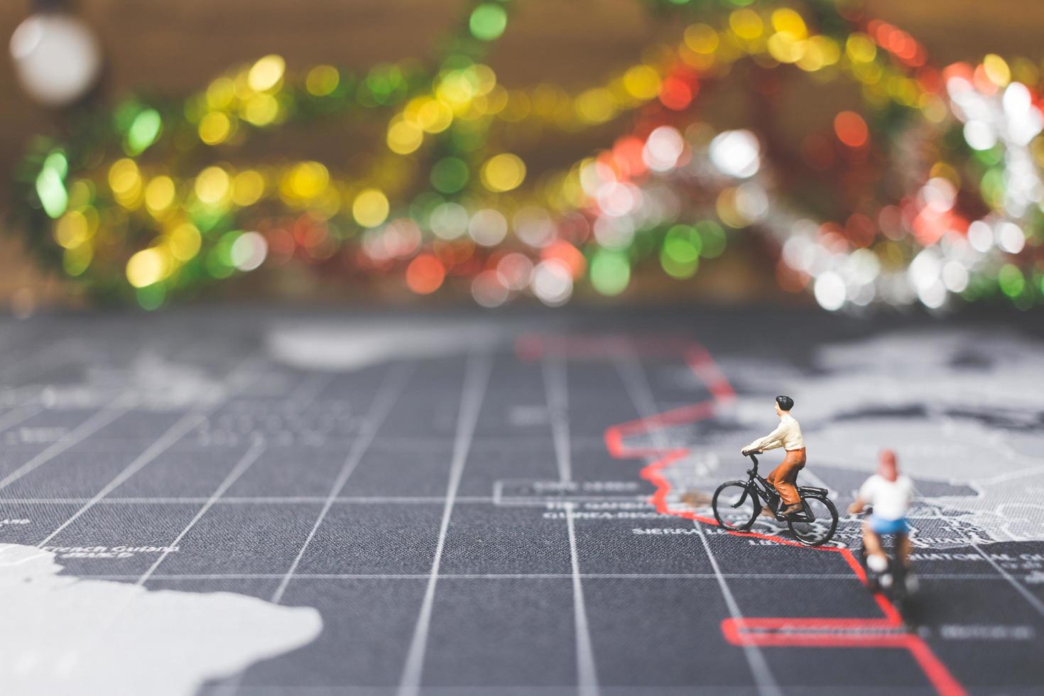 Miniaturreisende, die Fahrrad auf einer Weltkarte fahren, reisen und das Weltkonzept erkunden foto