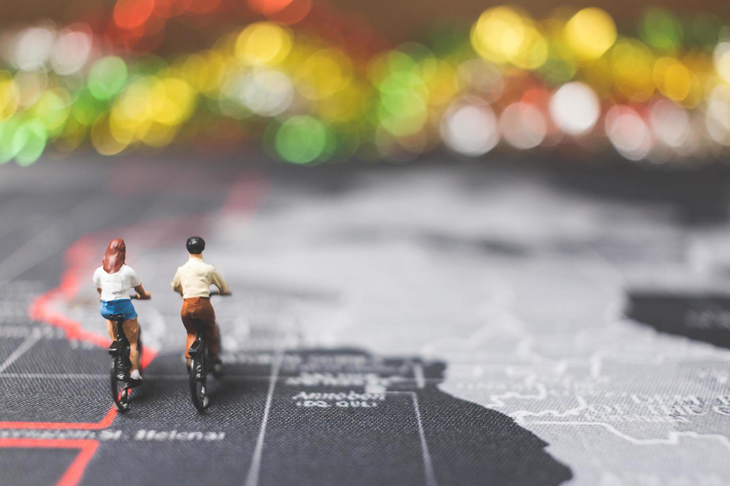 Miniaturreisende, die Fahrrad auf einer Weltkarte fahren, reisen und das Weltkonzept erkunden foto