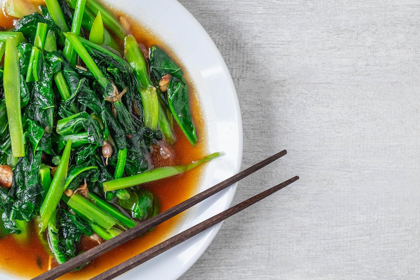 gebratener chinesischer Grünkohl mit Austernsauce mit Stäbchen auf einem weißen Teller auf Holztisch foto