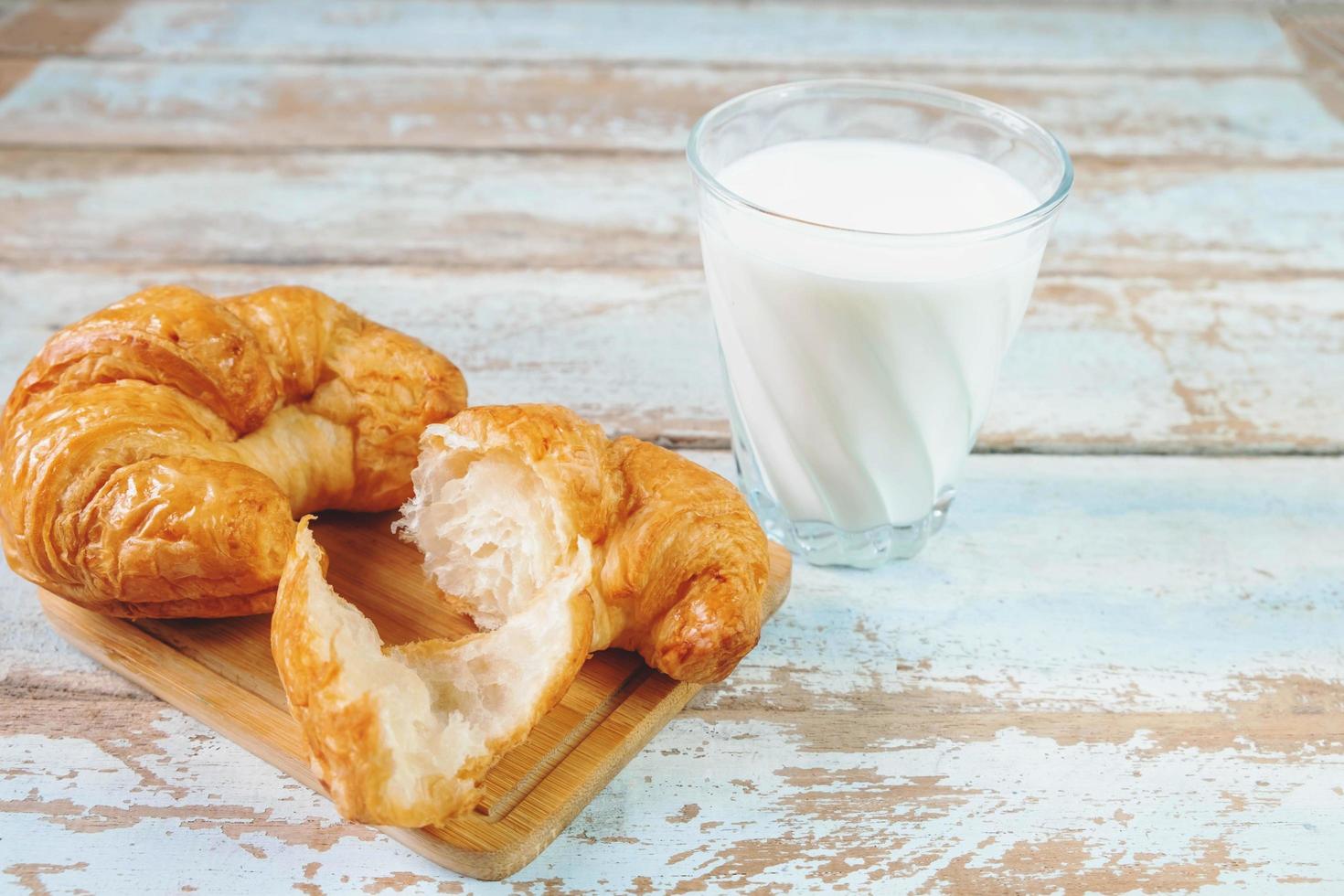 Croissants auf einem Holzschneidebrett neben Glas Milch auf blauem Holztisch foto