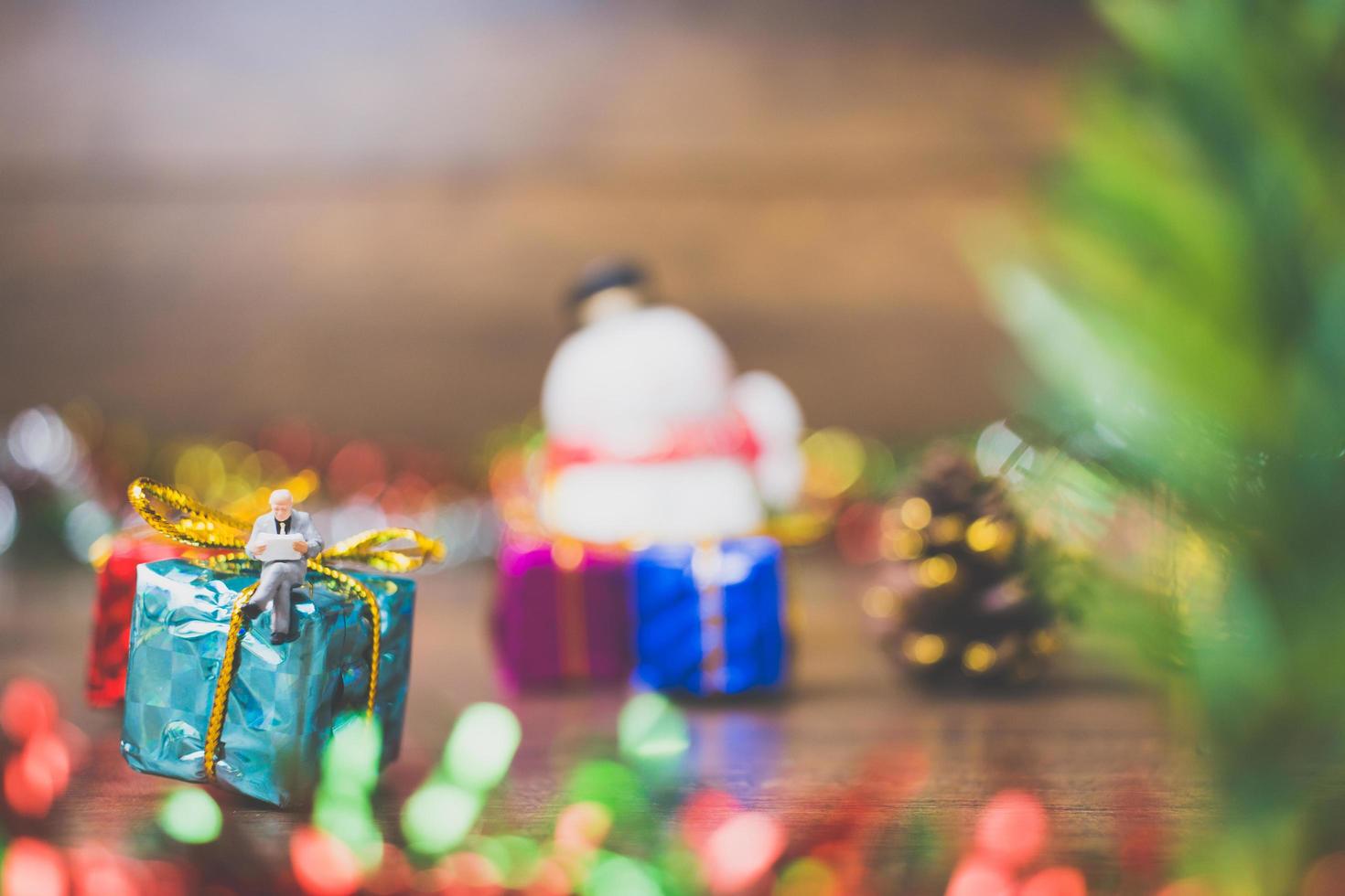 Miniaturperson auf einer Geschenkbox mit Weihnachtsfeierdekoration im Hintergrund foto