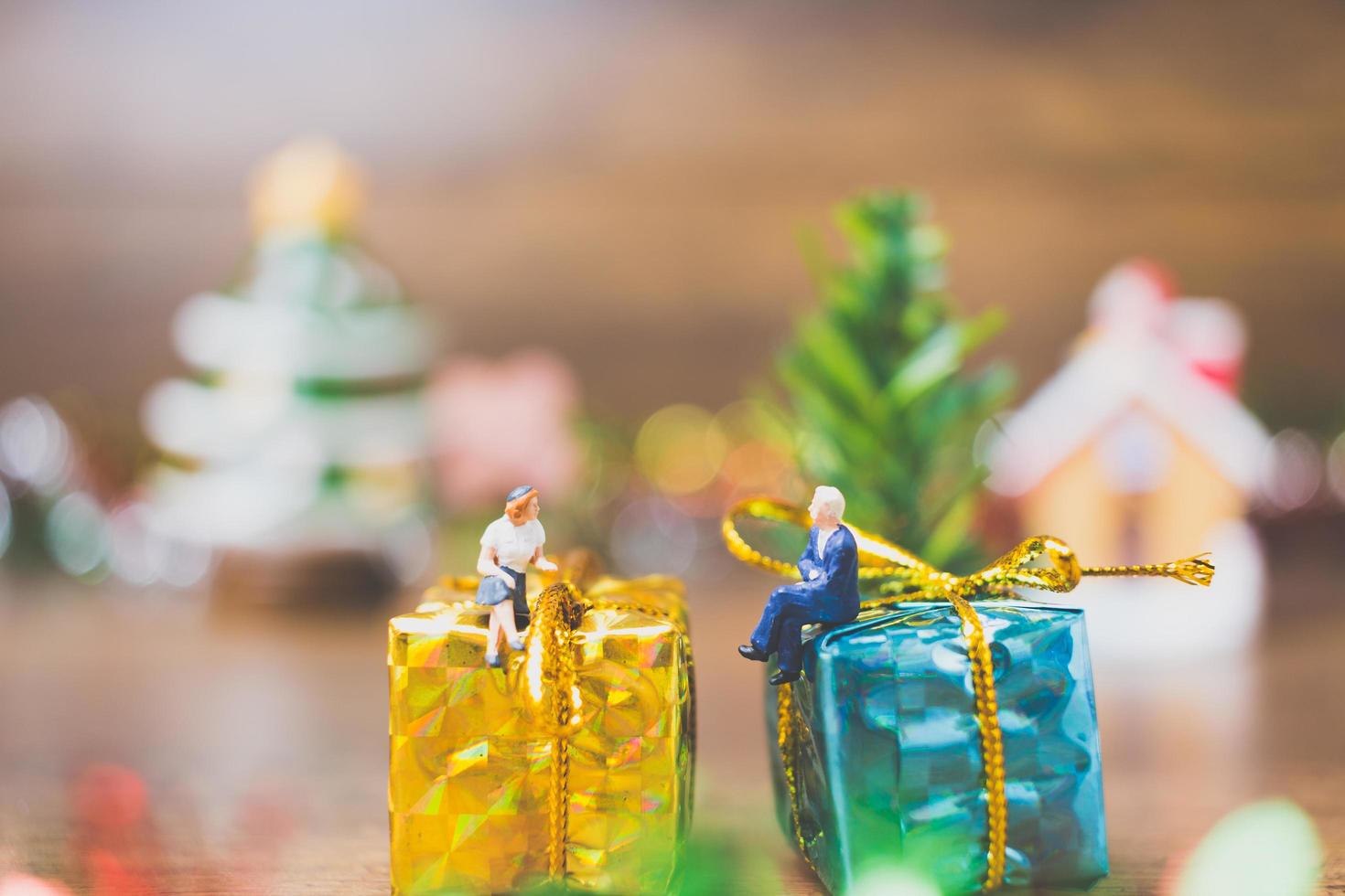 Miniaturmenschen auf einer Geschenkbox mit Weihnachtsfeierdekoration im Hintergrund foto