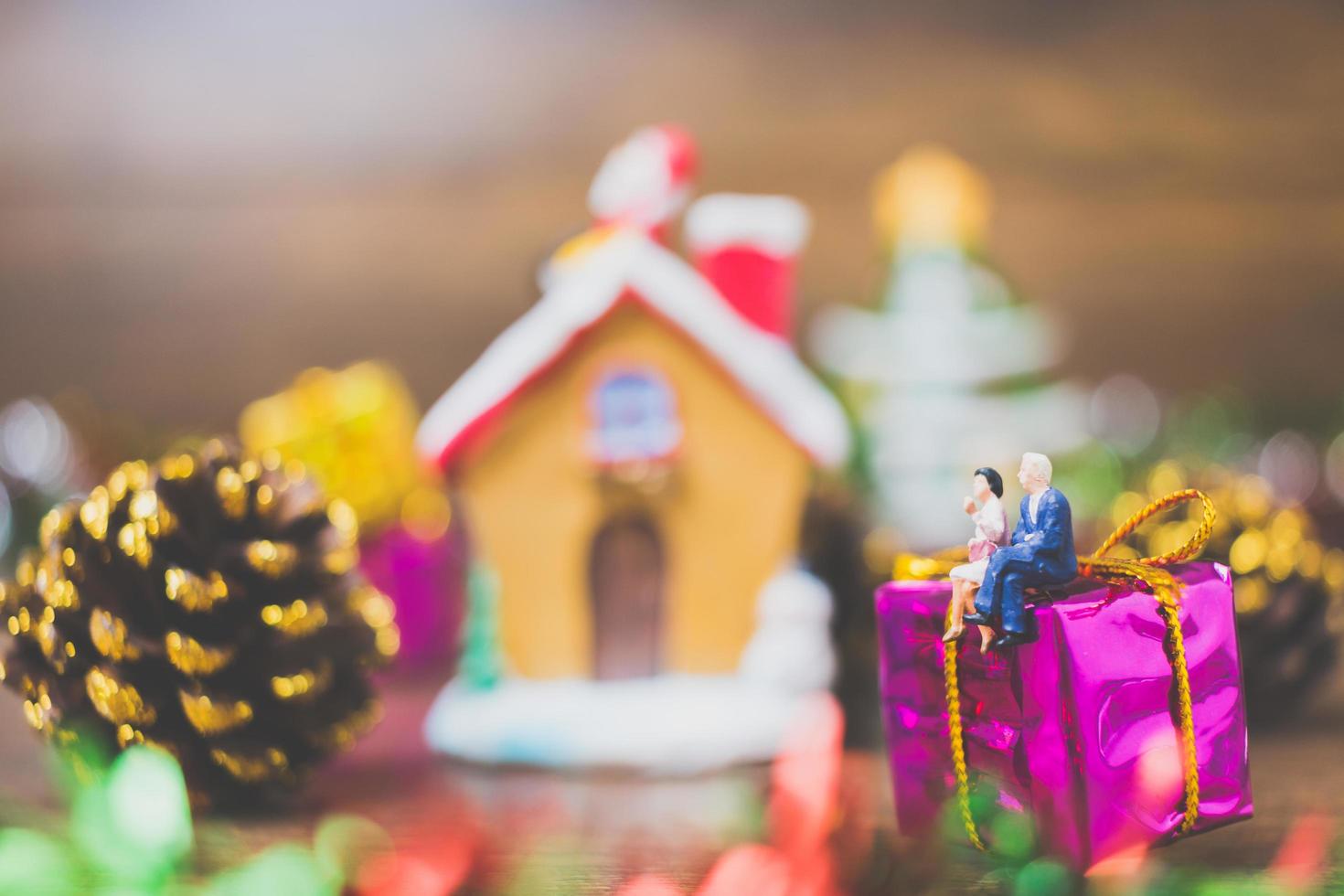 Miniaturmenschen auf einer Geschenkbox mit Weihnachtsfeierdekoration im Hintergrund foto