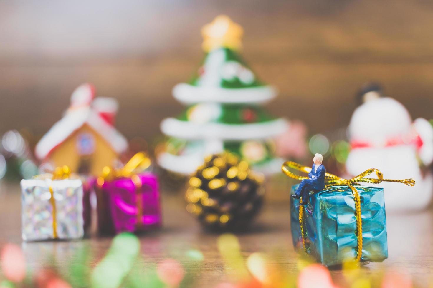 Miniaturperson auf einer Geschenkbox mit Weihnachtsfeierdekoration im Hintergrund foto