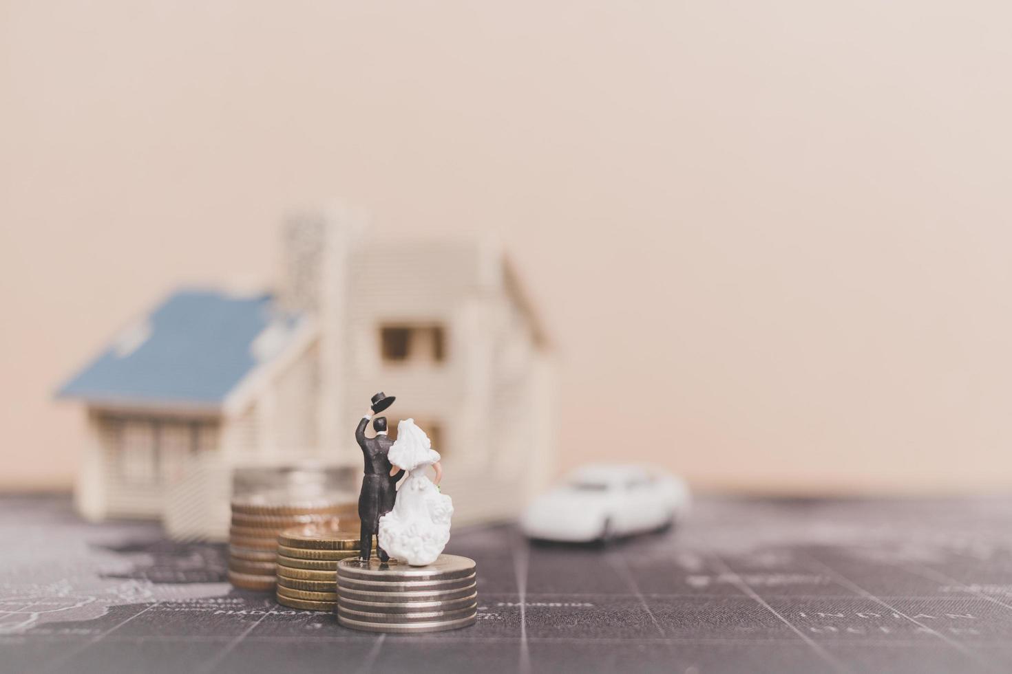 Miniatur Braut und Bräutigam mit Münzen vor einem Haus, erfolgreiches Familienkonzept foto