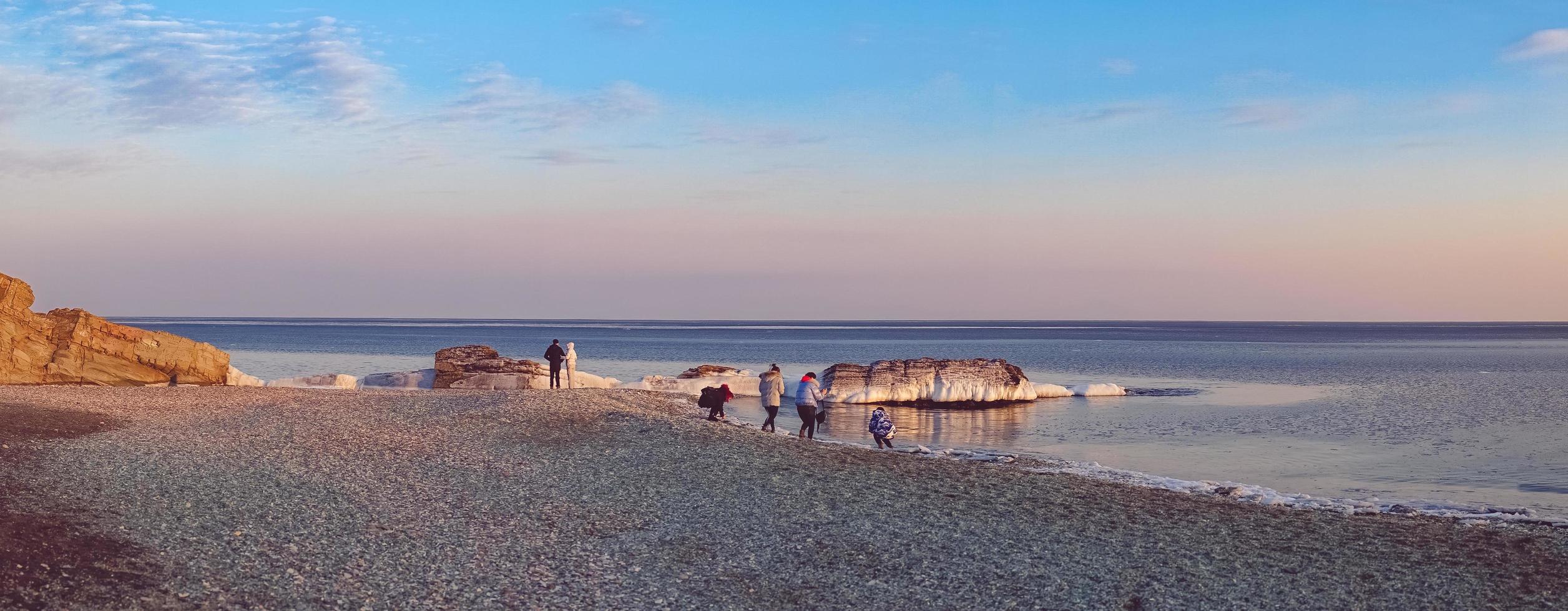 Panorama der Leute, die entlang Glasstrand gegen einen bunten bewölkten Himmel in Wladiwostok, Russland gehen foto