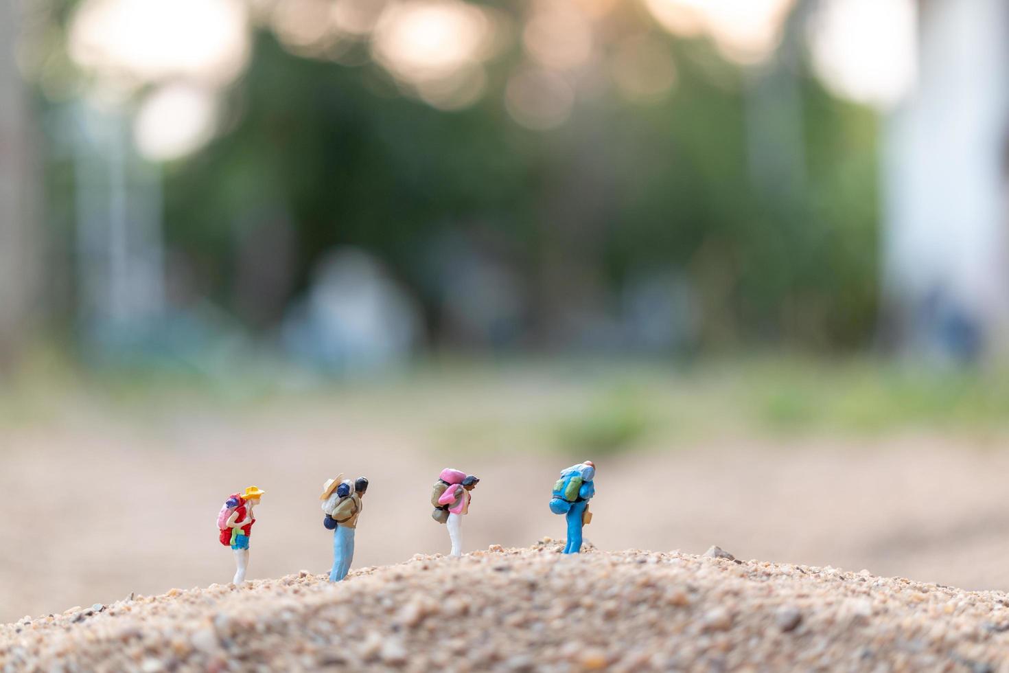 Miniaturreisende mit Rucksäcken auf Sand, Reise- und Abenteuerkonzept foto