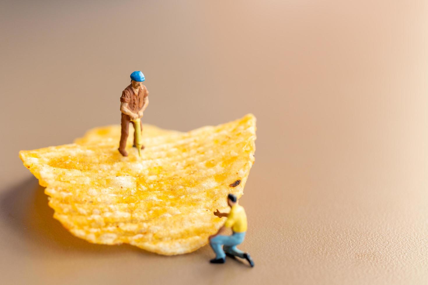 Miniaturarbeiter, die mit Kartoffelchips arbeiten foto