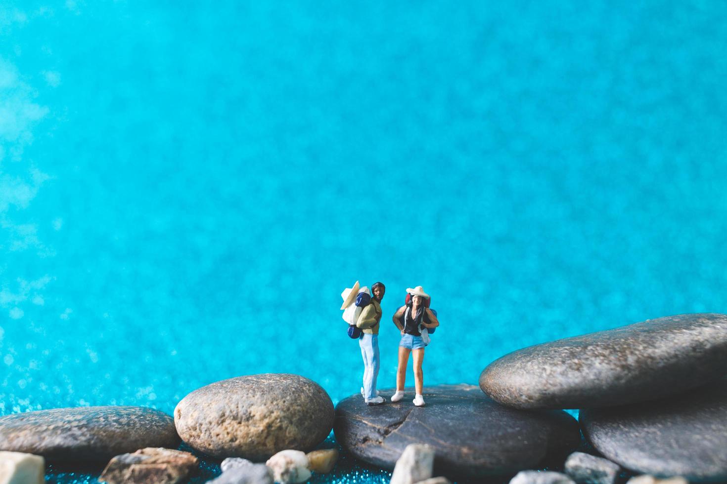 Miniatur-Rucksacktouristen, Touristen auf einem blauen Glitzerhintergrund foto