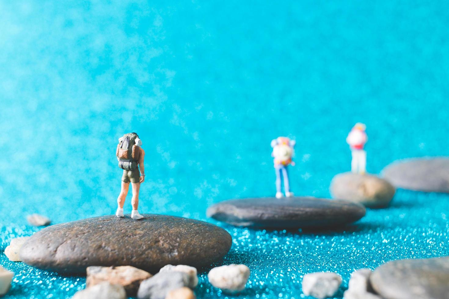 Miniatur-Rucksacktouristen, Touristen auf einem blauen Glitzerhintergrund foto