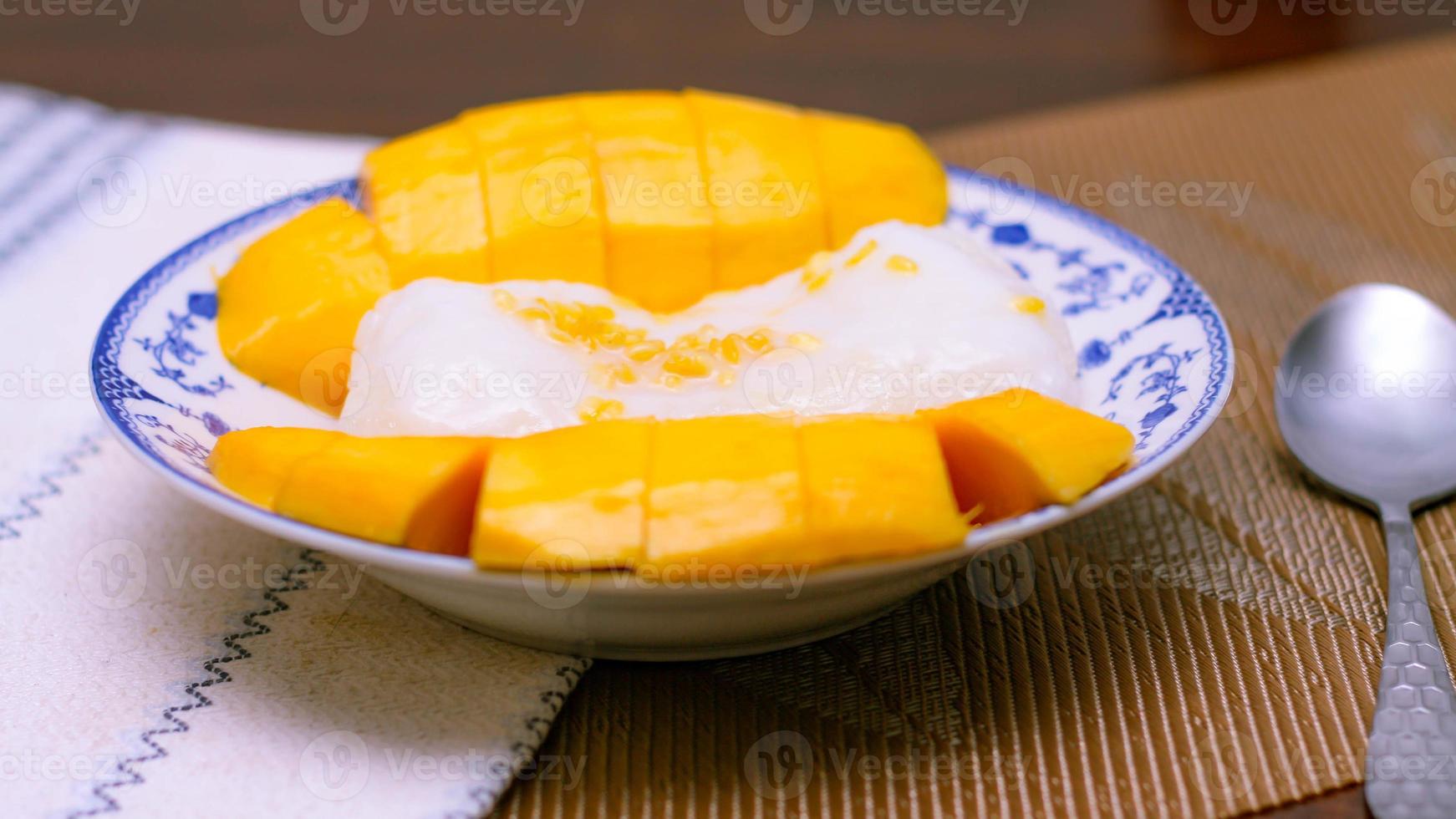 Mango klebrig Reis gekrönt mit Kokosnuss Milch und Sojabohnen platziert im ein traditionell Chinesisch Stil Gericht auf ein hölzern Tisch. foto