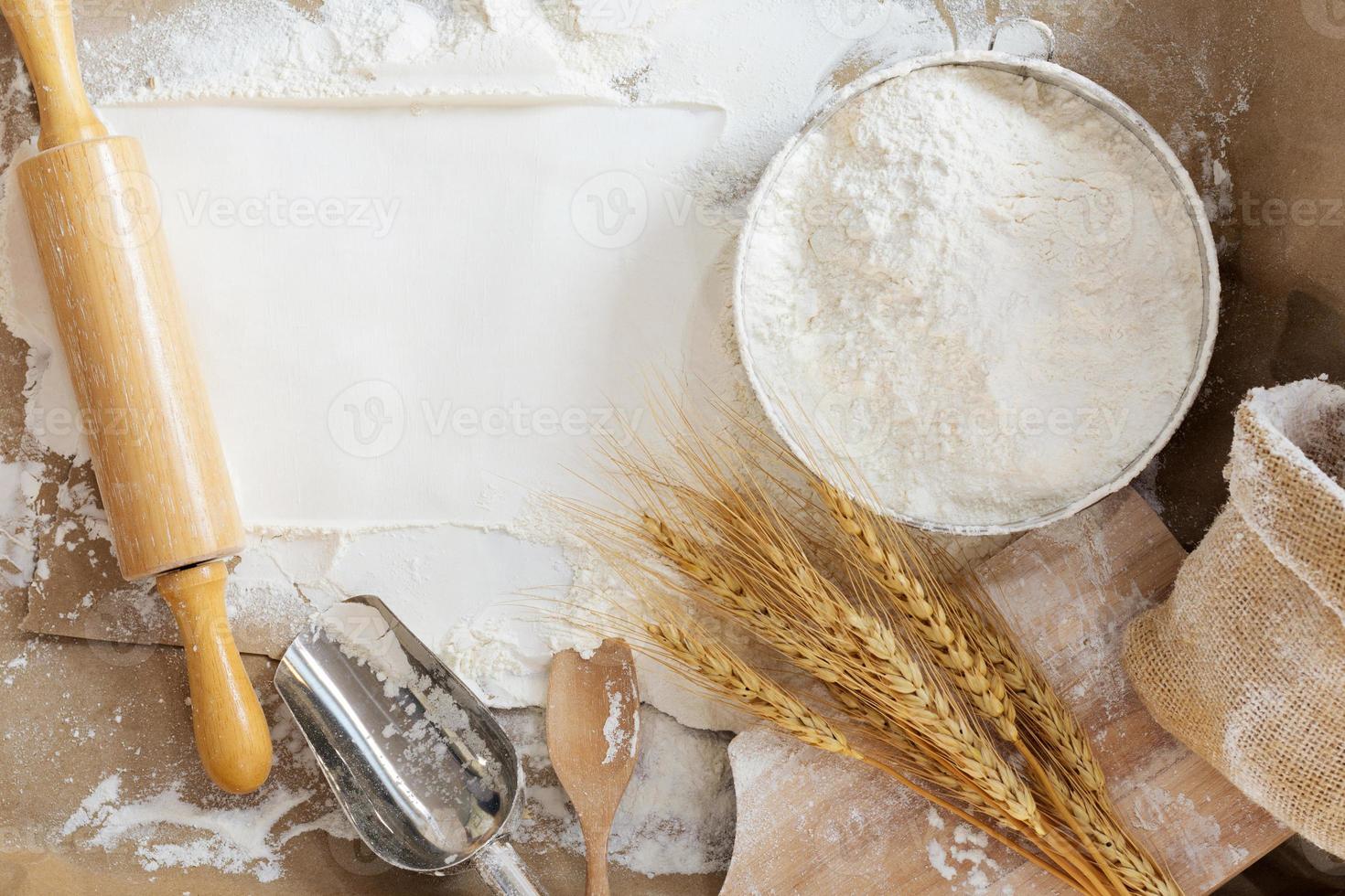 Mehl im ein Schüssel und Weizen Körner mit Weizen Ohren auf das Tisch, Papier Hintergrund im ein rustikal Küche, oben Aussicht foto