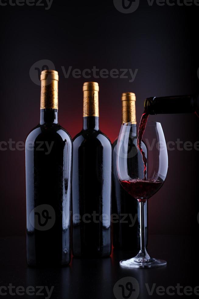 Weinflaschen und volles Glas mit rotem und schwarzem Hintergrund foto