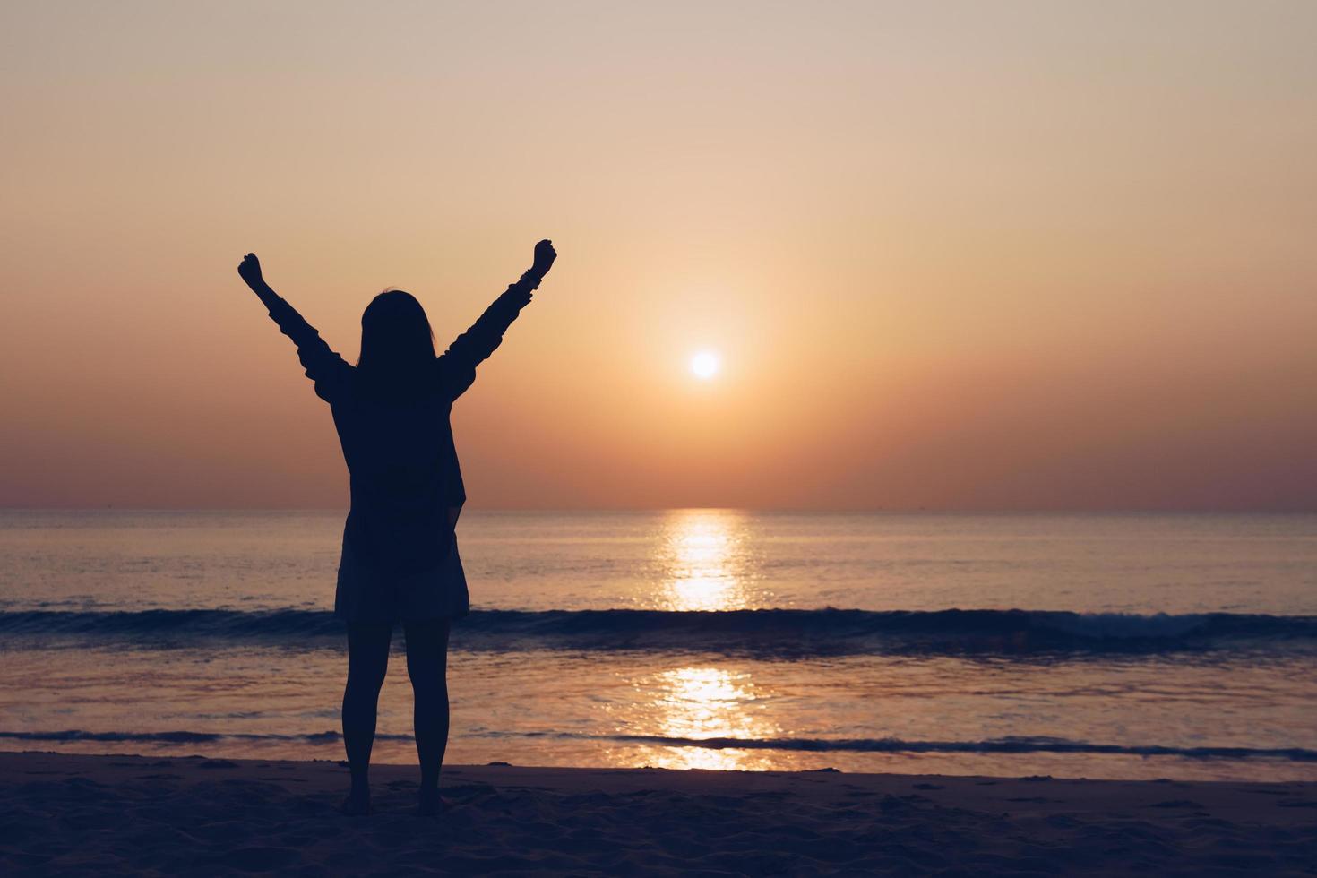 Frauensilhouette mit den Armen offen am Strand foto