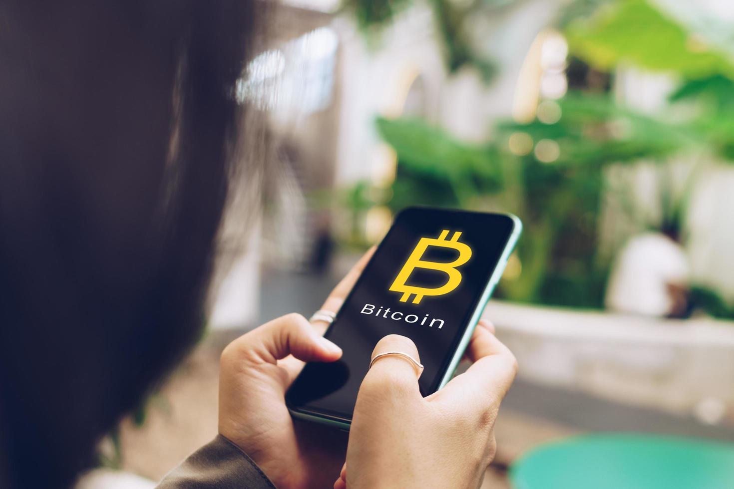 Frau nutzt mobiles Smartphone, um online mit Bitcoin Geld zu verdienen foto