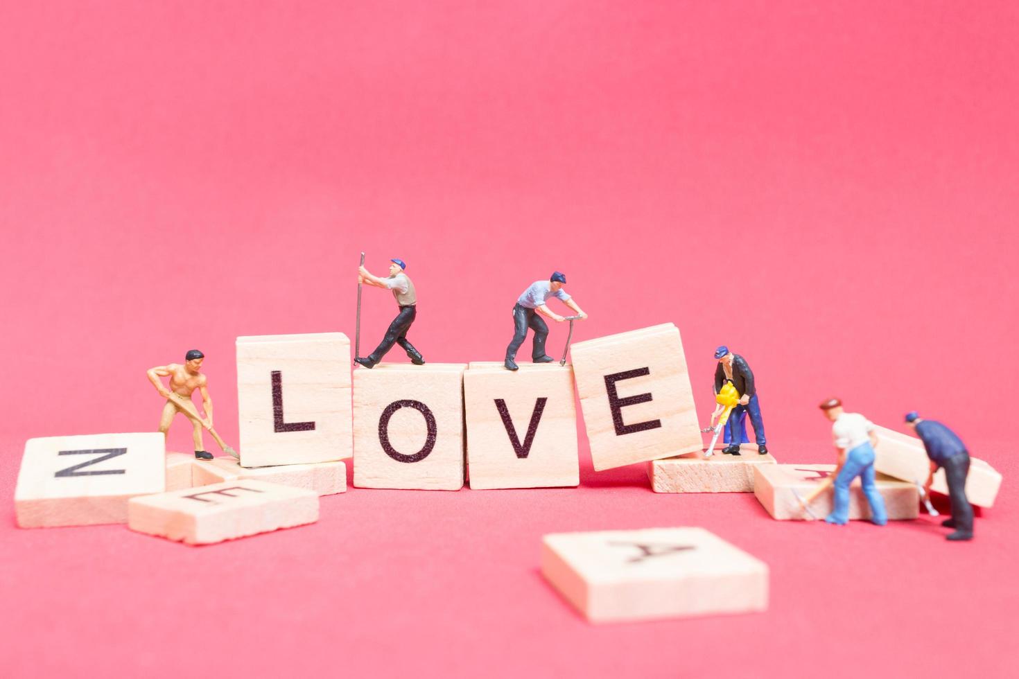 Miniaturarbeiter, die das Wort Liebe auf Holzklötzen mit einem rosa Hintergrund, Valentinstagskonzept bauen foto