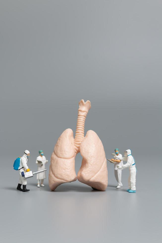 Miniaturärzte und Krankenschwestern, die das Konzept der menschlichen Lunge, des Virus und der mit Bakterien infizierten Menschen beobachten und diskutieren foto