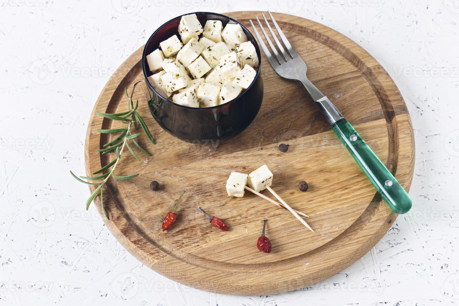 marinierter Feta auf einem Teller auf einem Holzbrett mit Gewürzen auf weißem Grund foto