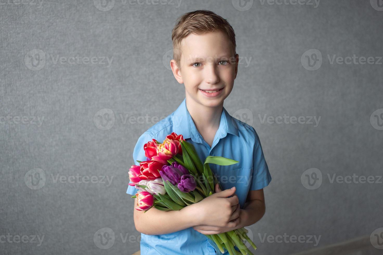 ein süß Junge im ein Hemd hält ein bunt Strauß von Tulpen im seine Hände. Raum zum Text foto