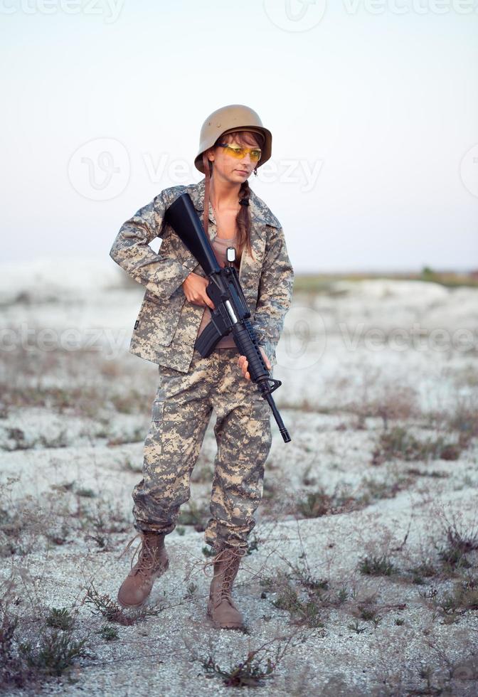 jung weiblich Soldat gekleidet im ein tarnen mit ein Gewehr im das draussen foto