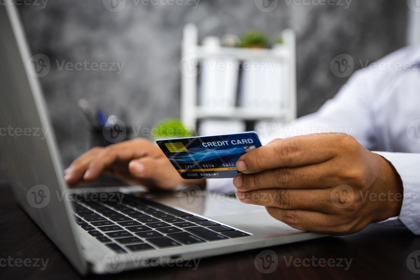 Nahaufnahmehand des Mannes, der Kreditkarte hält und am Laptop arbeitet foto