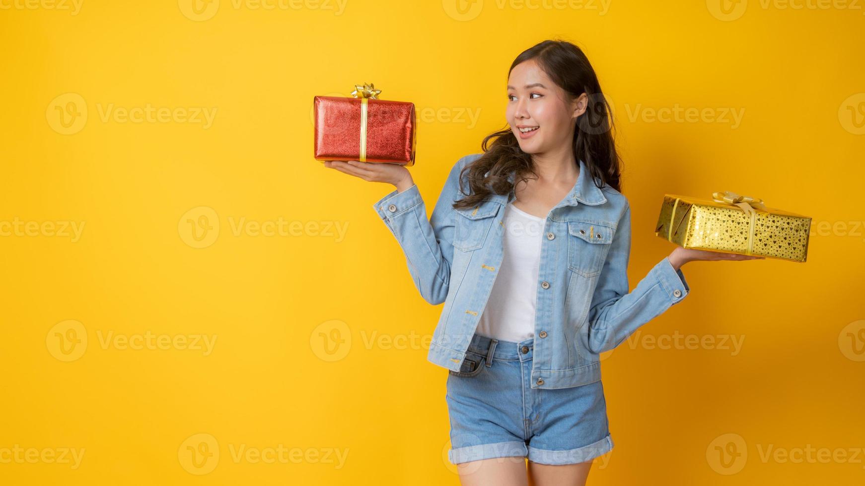 asiatische Frau, die rote und goldene Geschenkboxen auf gelbem Hintergrund hält foto