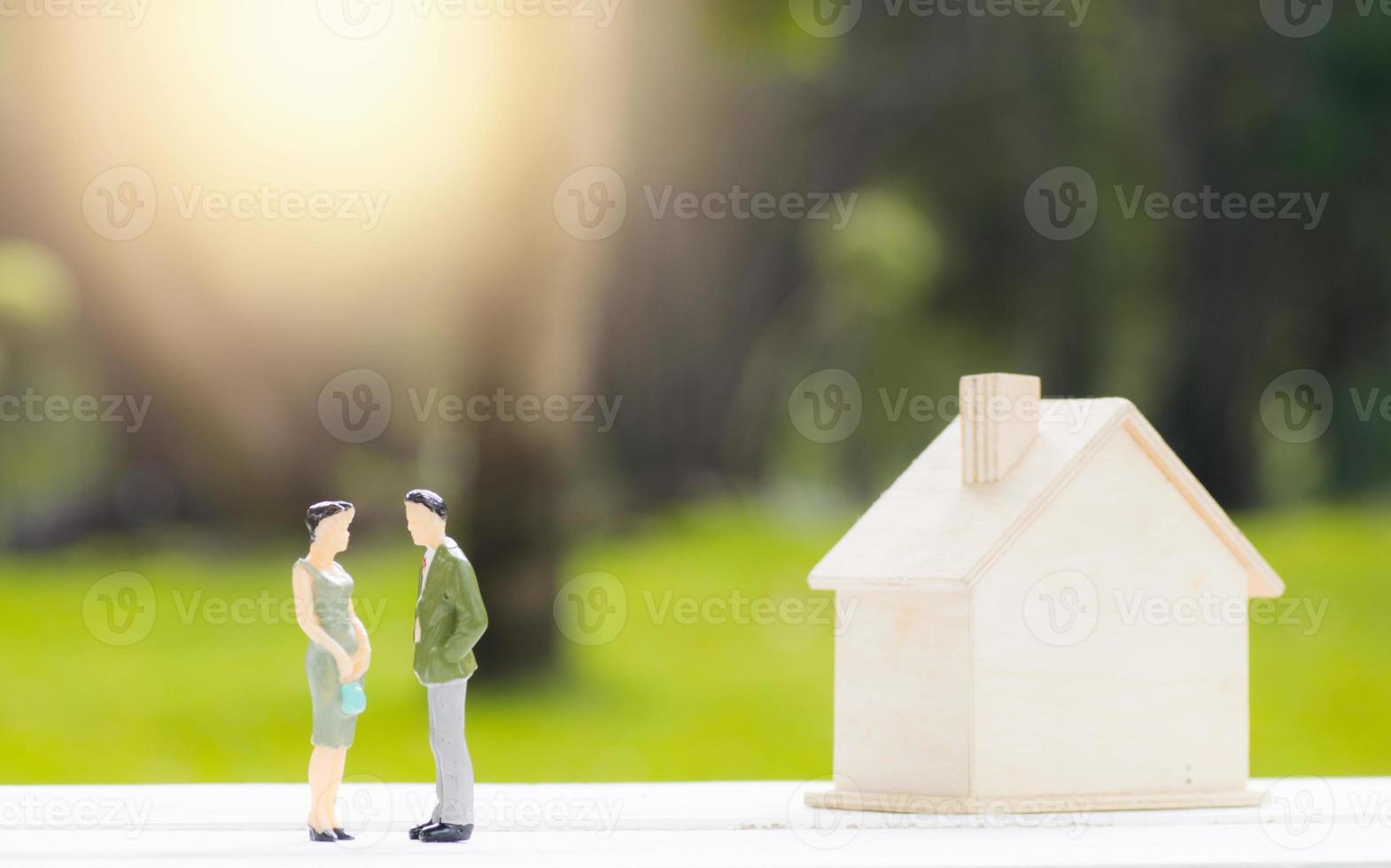 Miniaturfiguren des Mannes und der Frau neben Modellhaus mit unscharfem Naturhintergrund foto